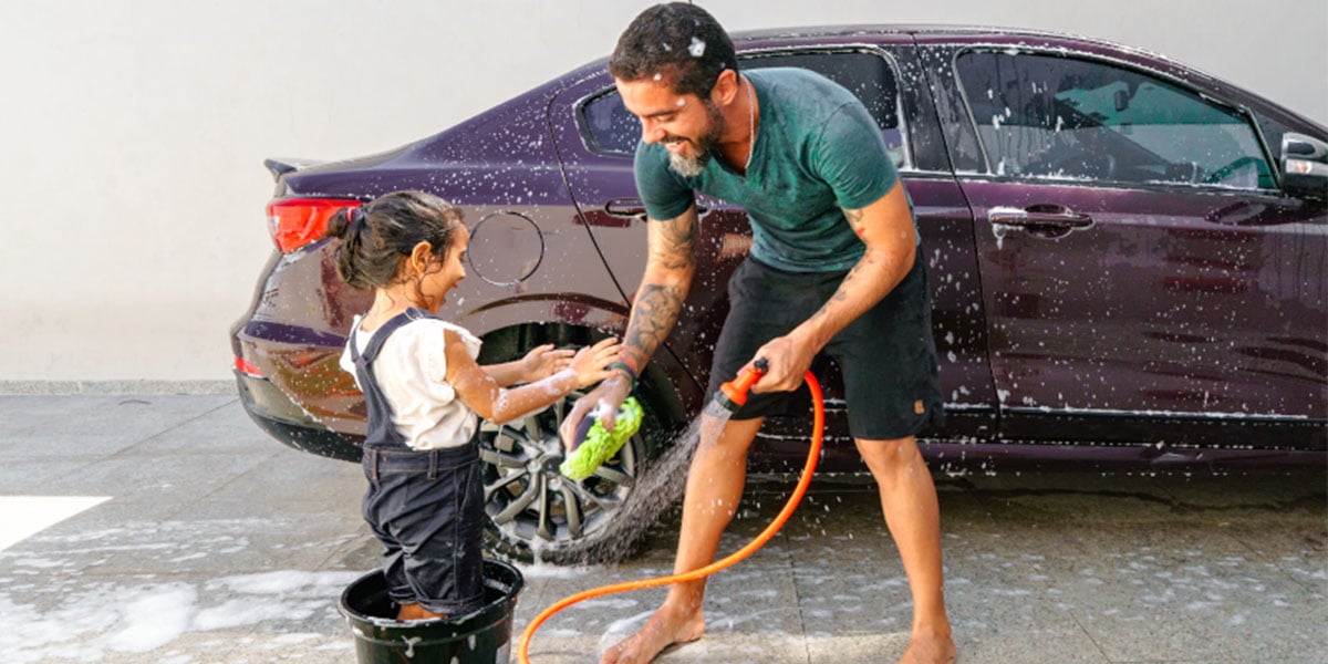 Vater und Tochter waschen mit viel Freunde ein violettes Auto mit dem Gartenschlauch | Zurich Connect Kfz-Versicherung