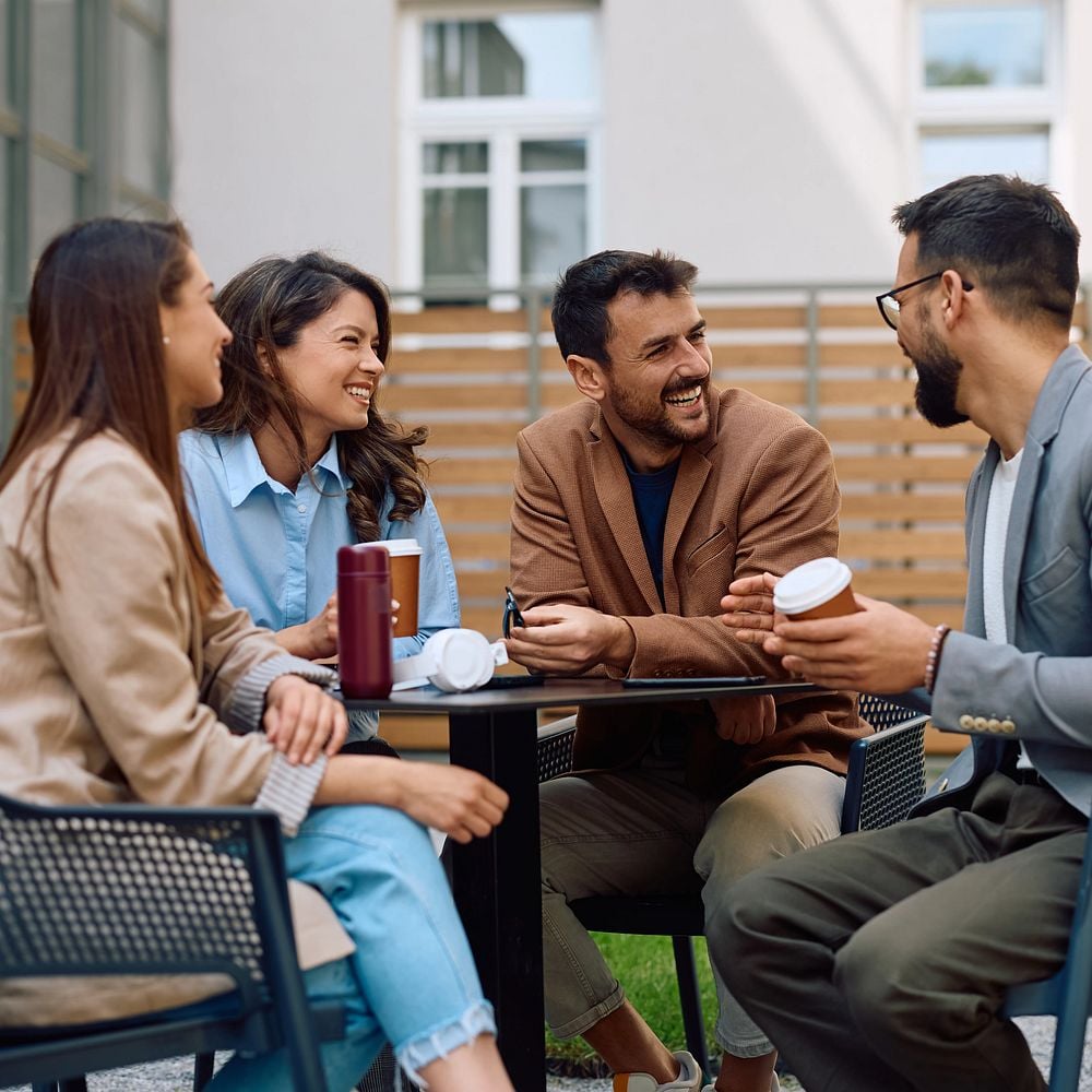 Cheerful coworkers drinking coffee and communicating at office building patio