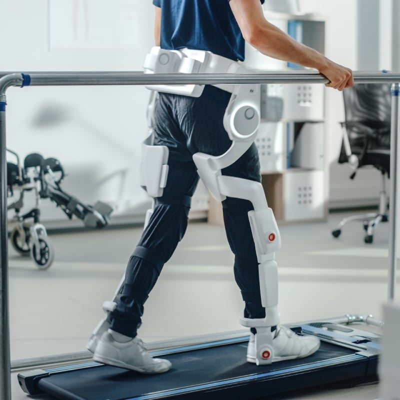Person walking with robotic exoskeleton on treadmill.