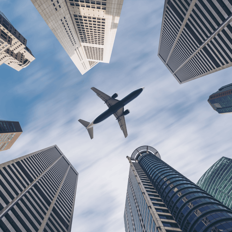 Airplane flying above tall city buildings.