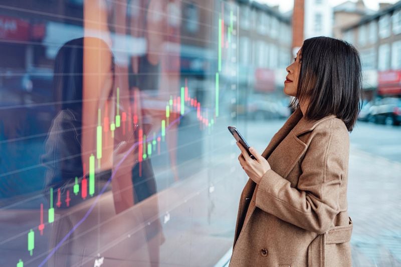 Young Asian businesswoman looking at stock exchange market trading board
