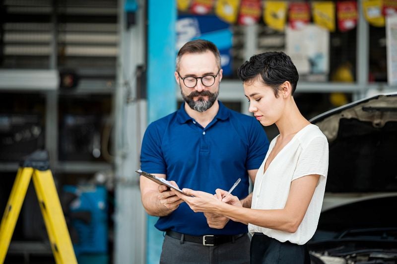 Female customer sign accept on car repair checklist or claim form with auto mechanic at Auto Repair Center
