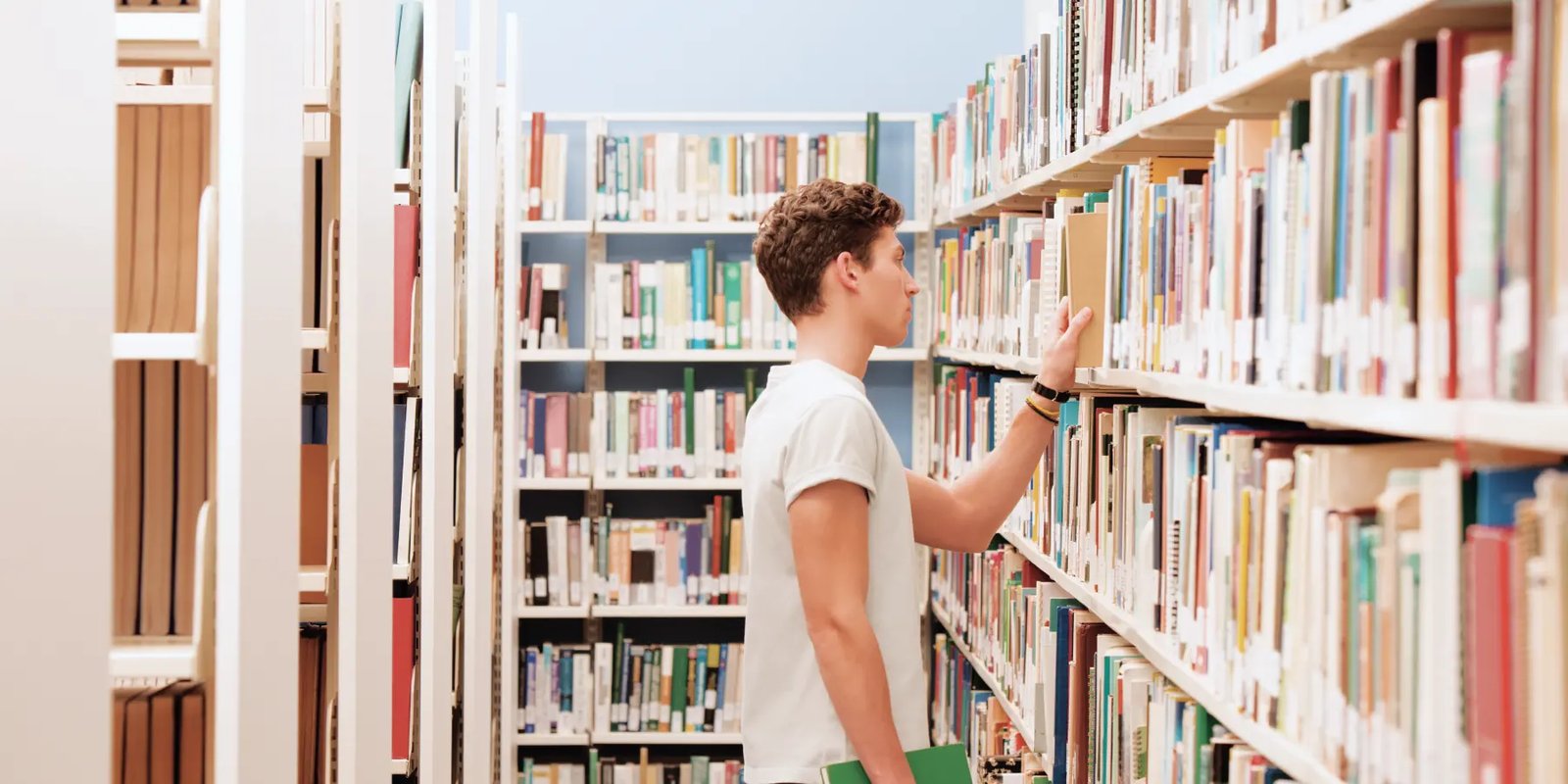 Estudante concentrado em seus estudos em uma biblioteca escolar, com livros ao fundo. A imagem representa o foco e a concentração que a nova lei busca promover ao restringir o uso de celulares nas escolas