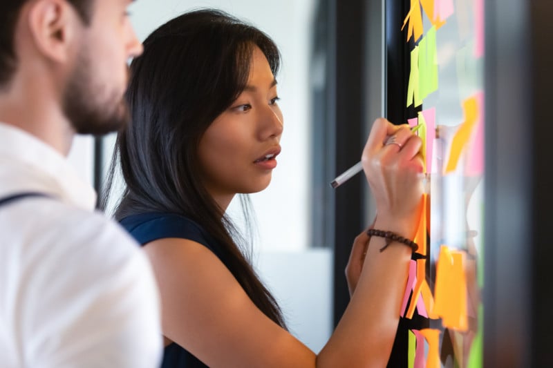 Asian woman writing on a glass panel full of post-its.