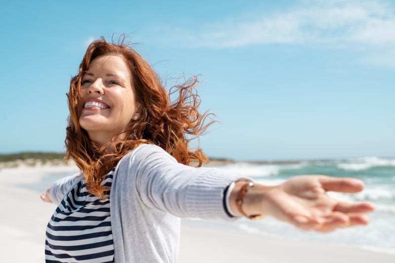 Woman with a smile on her face spreading her arm open at a beach