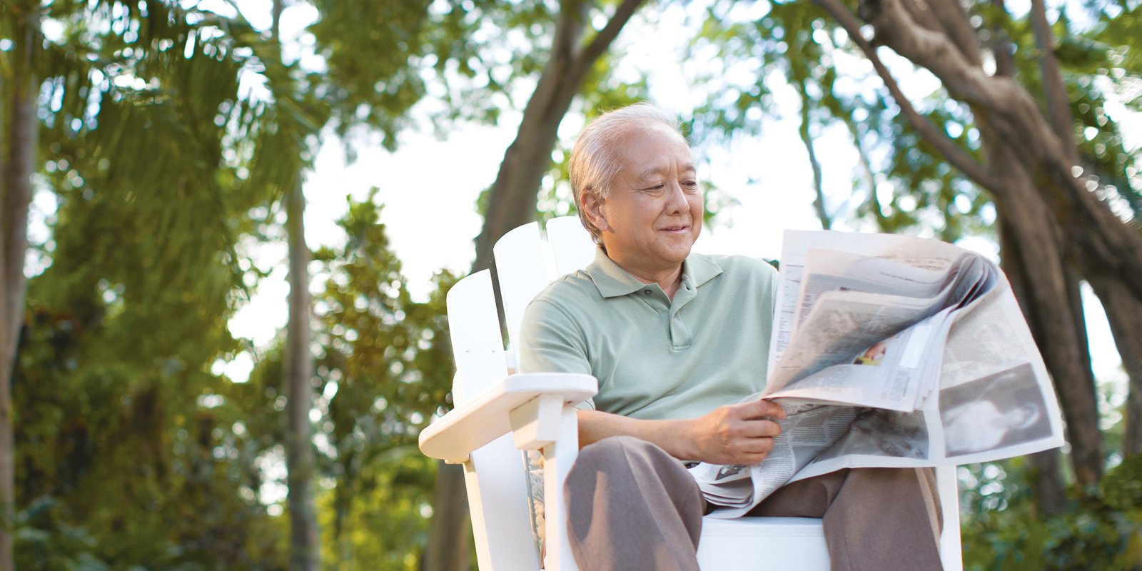 Older man reading newspaper in garden sitting on a chair