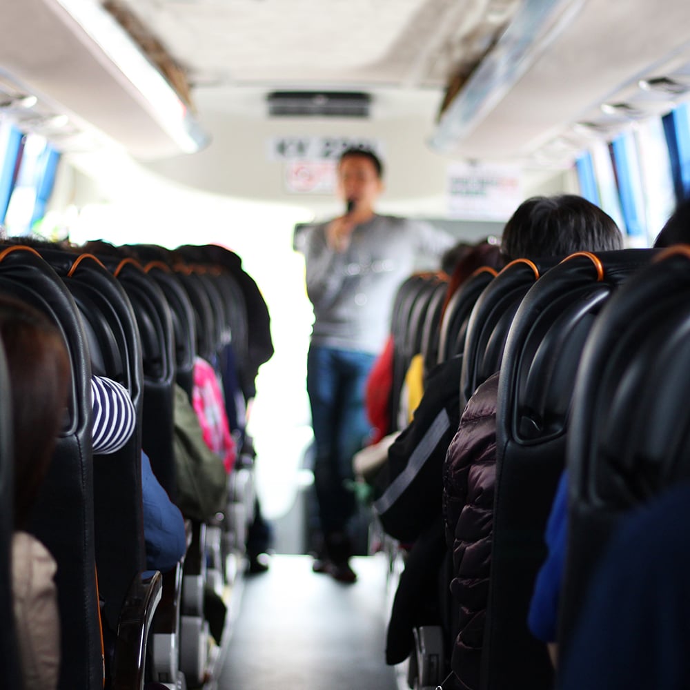A tour guide is talking to the tourists at a travel bus