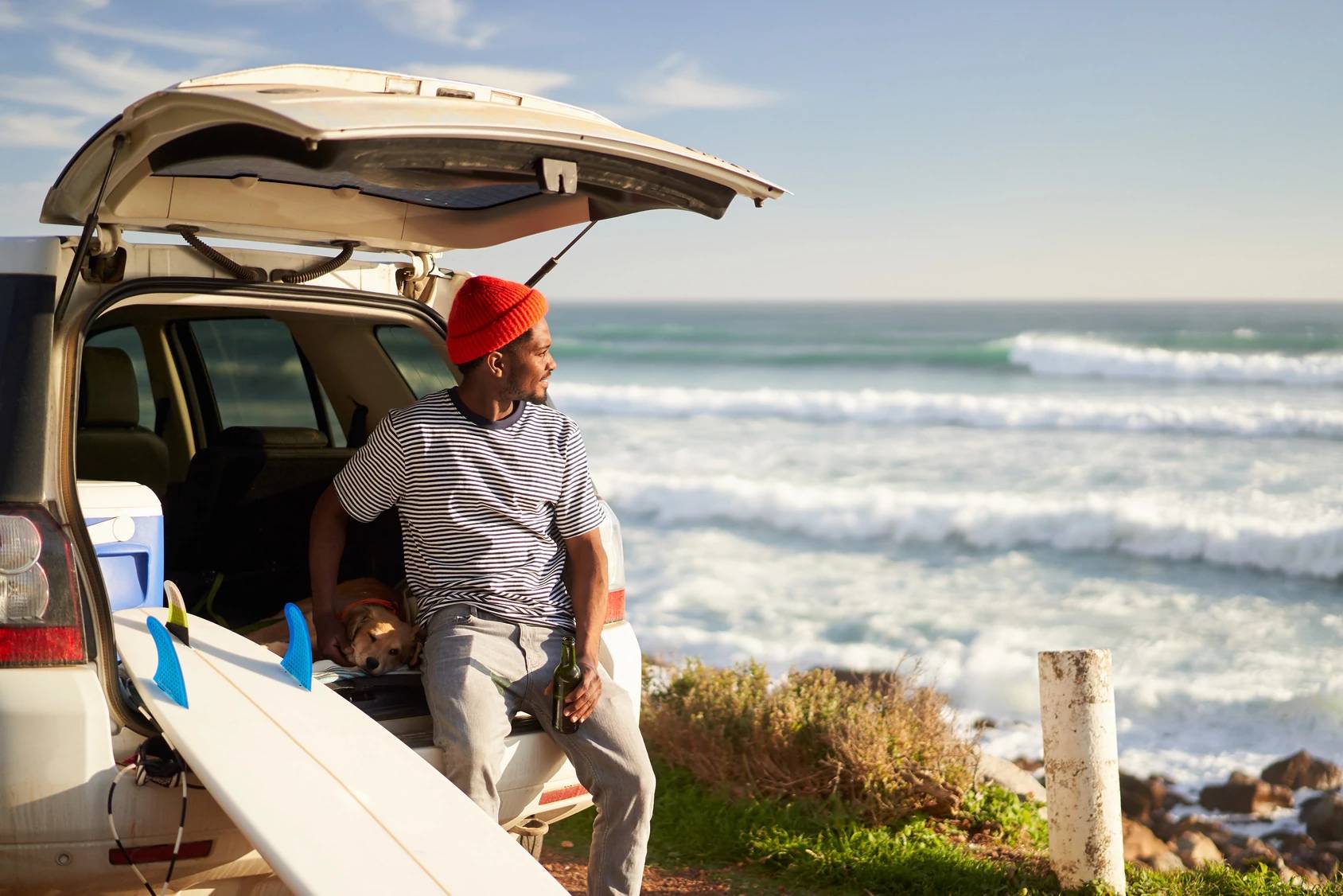 Man leaning on a vehicle near the sea.