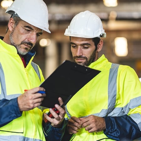 Workers in safety gear reviewing clipboard.