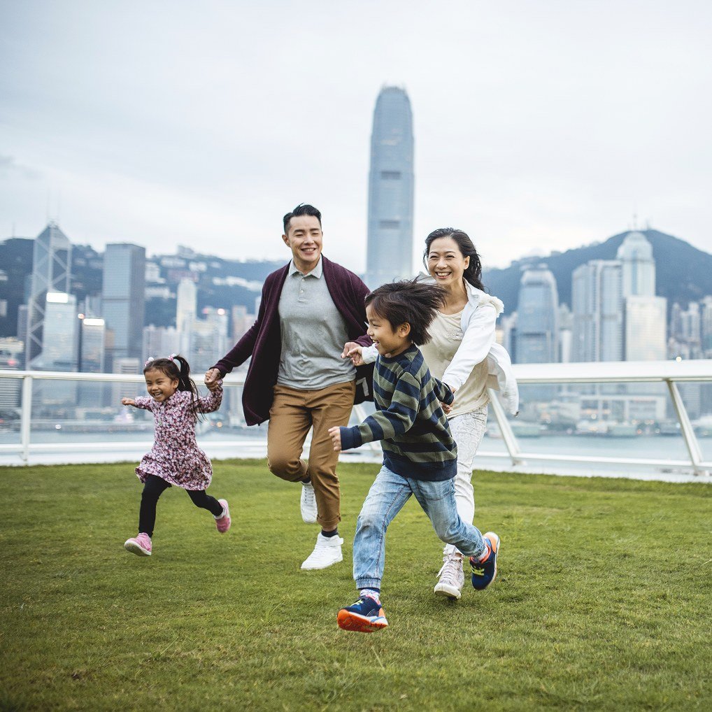 Family running on grass with city skyline.