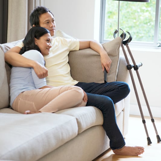 Couple relaxing on sofa with crutches nearby.