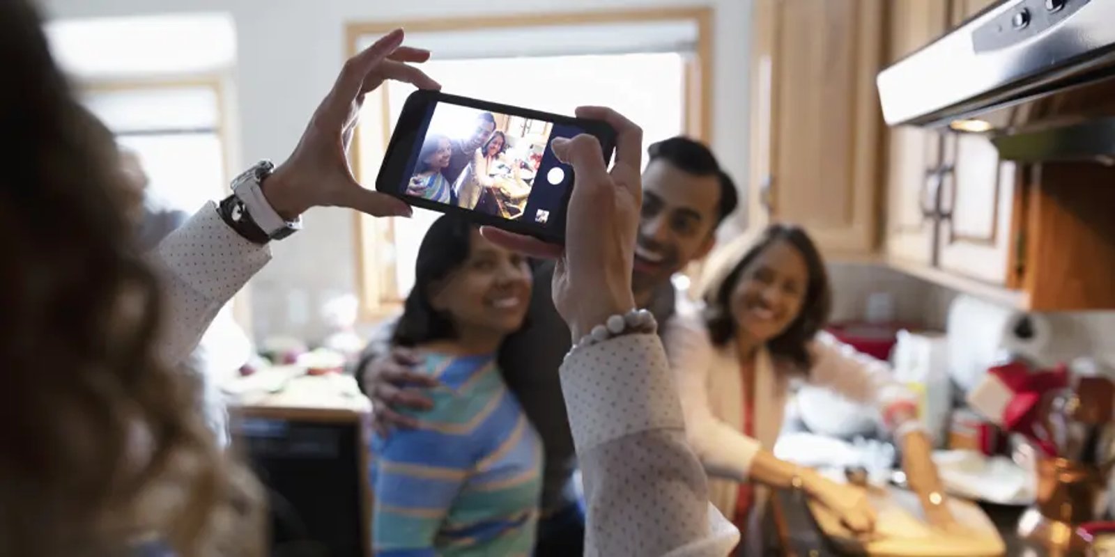 Woman with smartphone photographing family cooking