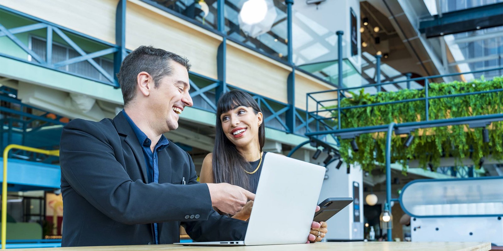 Businessman and businesswoman looking at the report from laptop computer while working in sustainable workplace with green plant for business