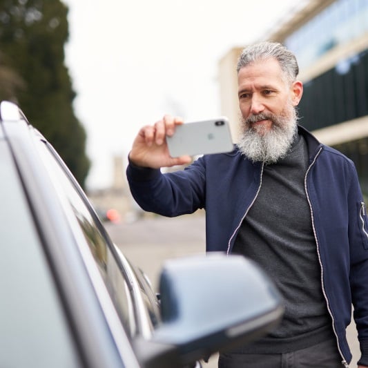 Ein Mann macht Fotos von seinem Auto mit dem Smartphone