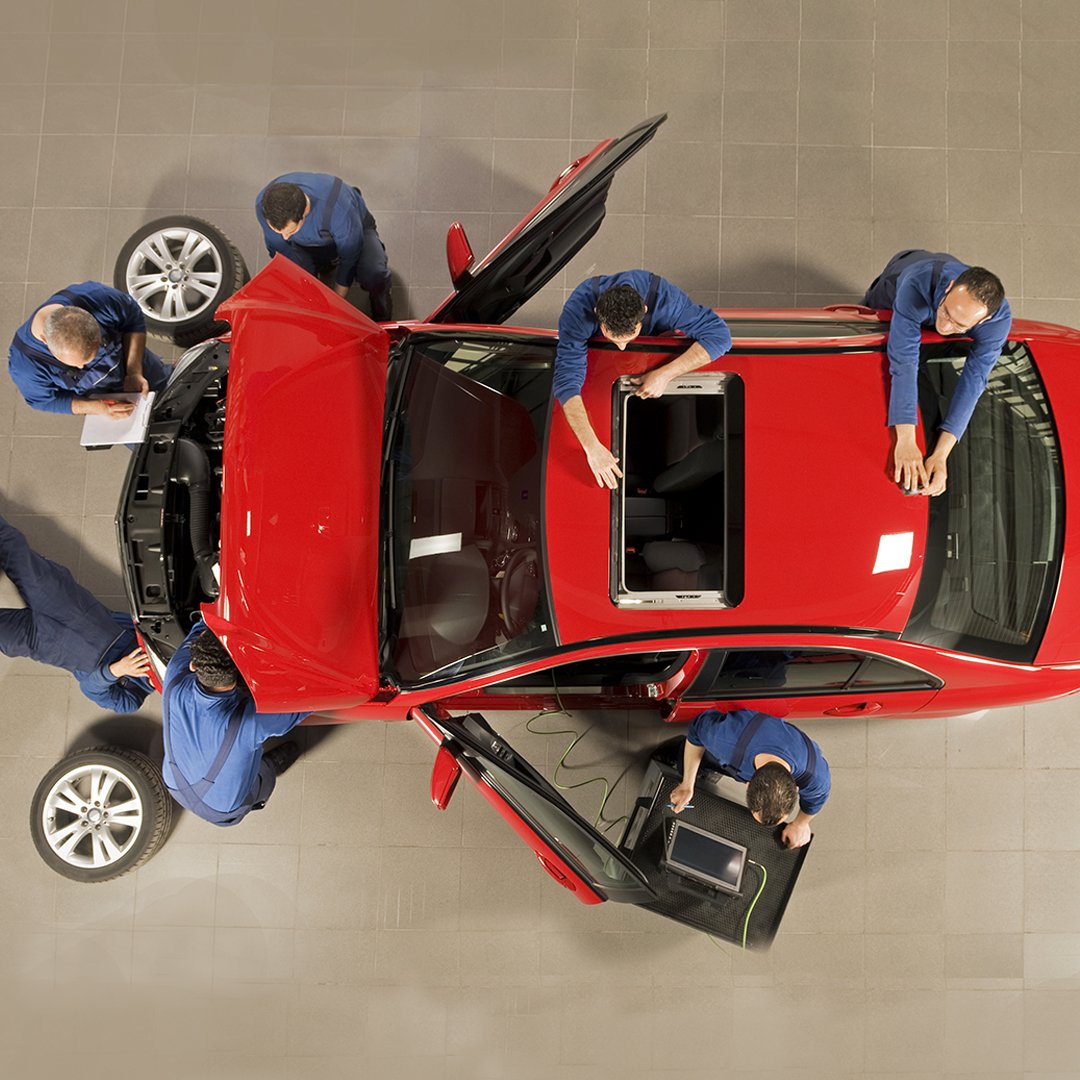 1080x1080_smart_easy Rotes Auto wird von mehreren Mechanikern in der Werkstatt repariert