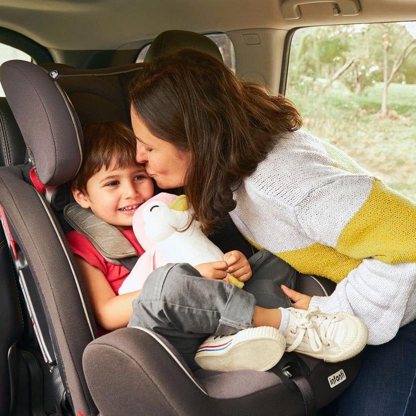 Mutter küsst ihren Sohn im Kindersitz im Auto