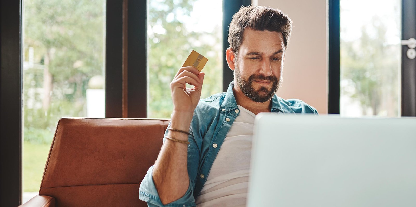 Mann sitzt mit gezückter Kreditkarte vorm Laptop