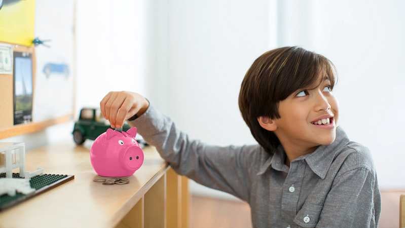 Ein Junge schmeißt Münzen in ein rosa Sparschwein