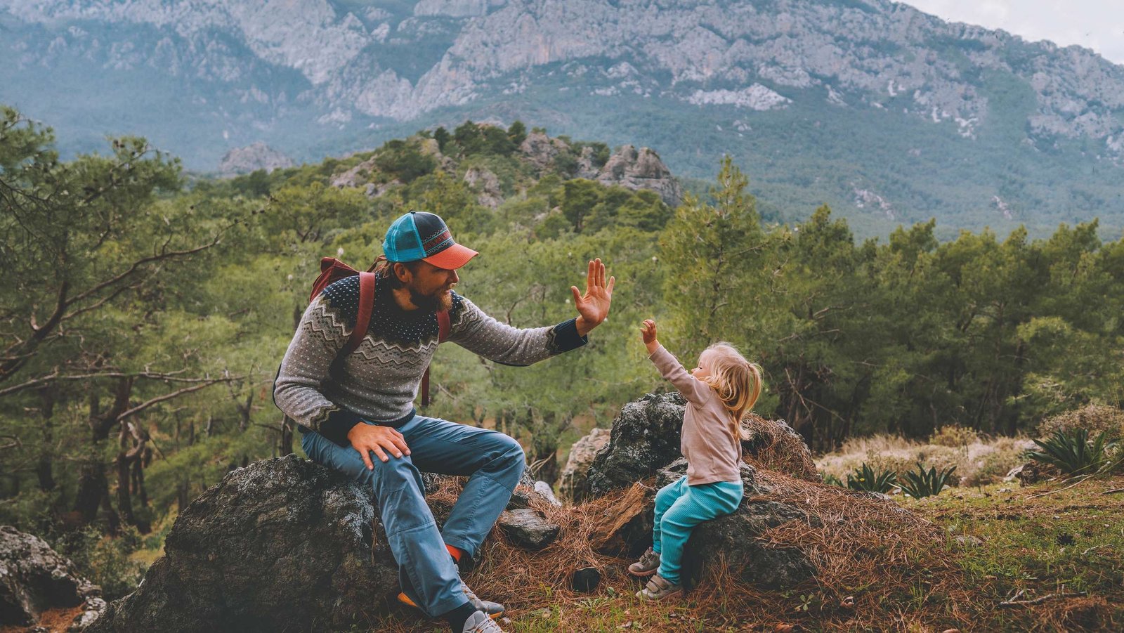 Vater und Tochter sitzen am Berg und geben ich Hight Five.