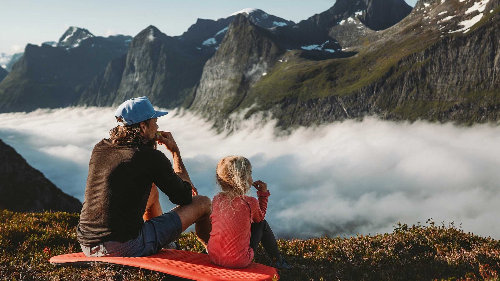 Vater und Tochter sitzen am Berggipfel und schauen in die Ferne | Zurich Unfallversicherung