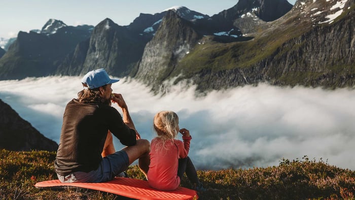 Vater und Tochter sitzen am Berggipfel und schauen in die Ferne | Zurich Unfallversicherung