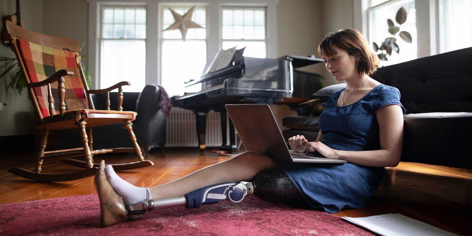 Eine Frau mit Beinprothese sitzt am Boden und schaut etwas am Laptop nach