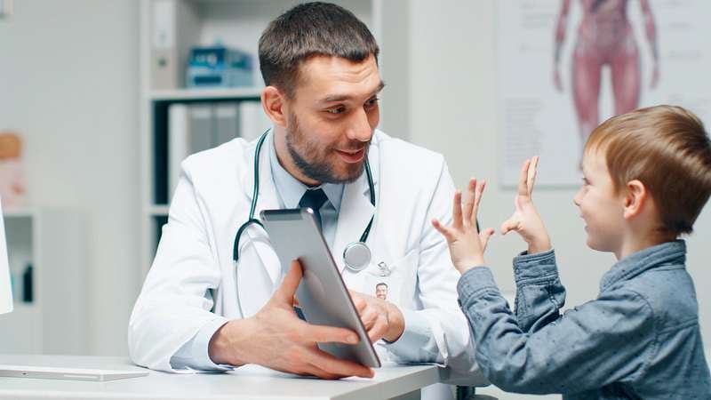 Ein Kind sitzt beim Arzt und zeigt mit den Fingern zu ihm.