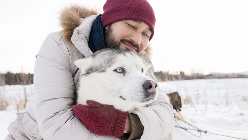 Mann umarmt Husky in Winterlandschaft