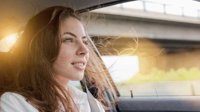 Eine Dame sitzt lächelnd im Auto und die Sonne geht im Hintergrund unter.