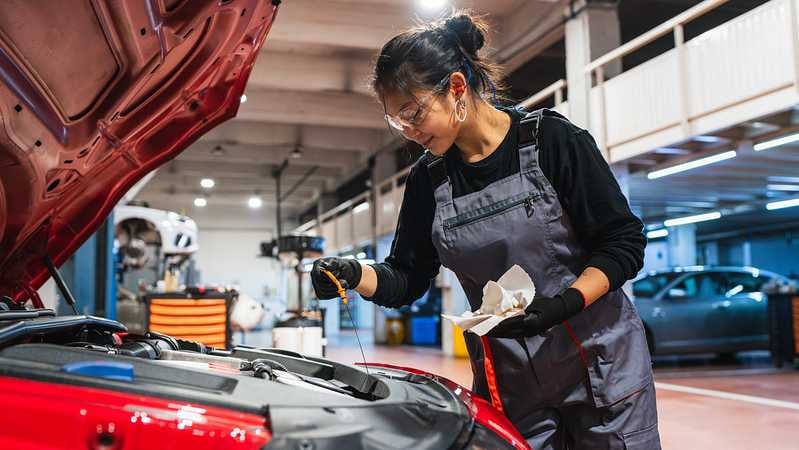 eine mechanikerin überprüft den Ölstand beim Auto in der Werkstatt