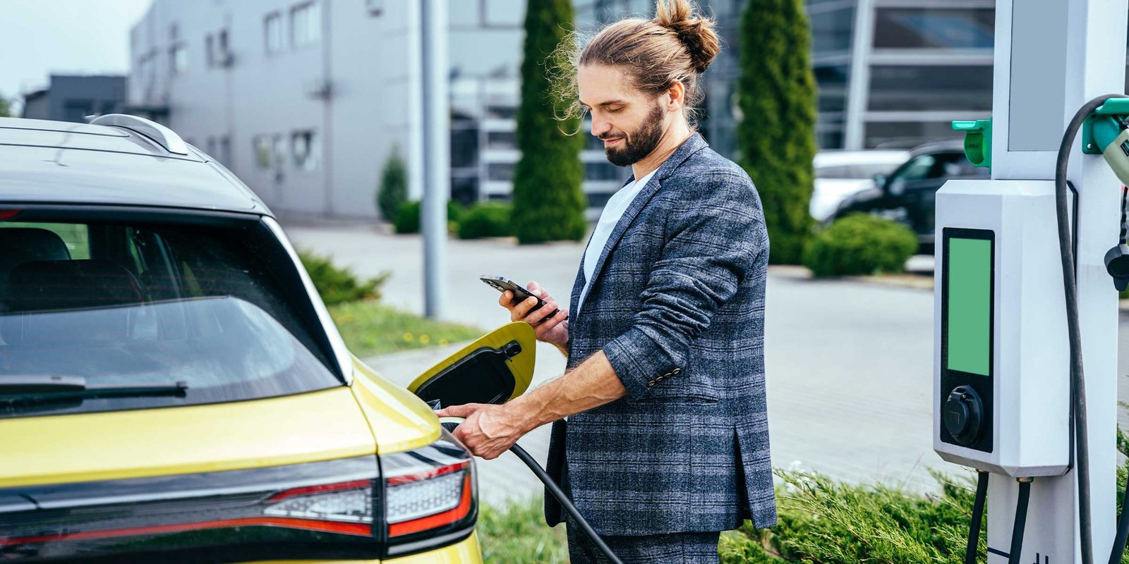 Mann steht beim E-Auto und öffnet die App zum Laden