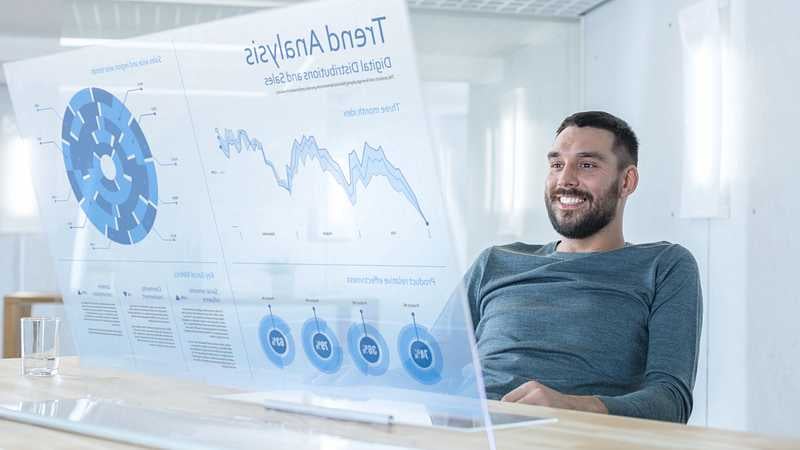 Ein Mann sitzt vor futuristischen Bildschirm und prüft Zahlen.