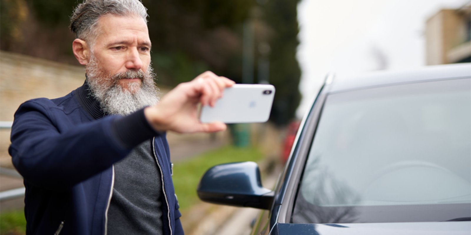 Mann fotografiert mit Handy einen Blechschaden an seinem Auto