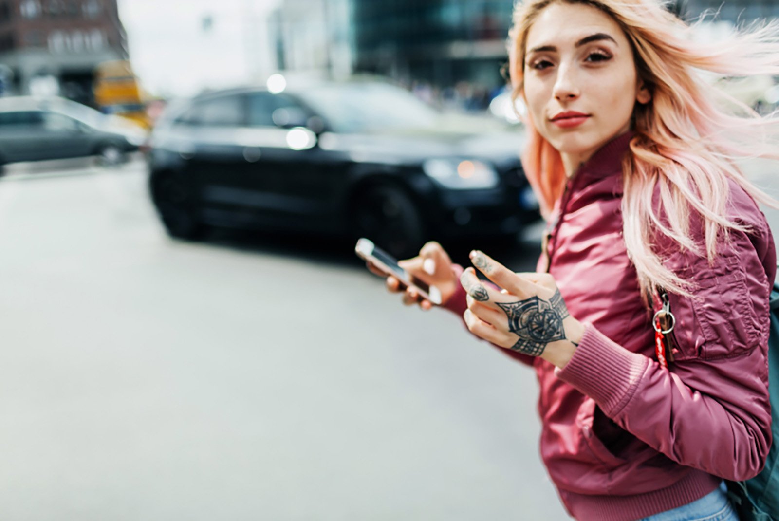Dame mit roter Jacke hat ein Handy in der Hand und läuft über die Straße