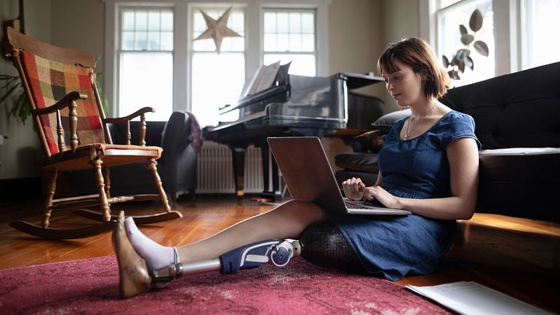 Dame mit Prothese sitzt am Boden und schreit am Laptop.