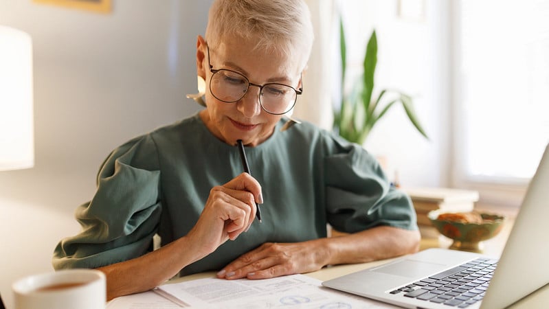 Eine ältere Dame sitzt am Tisch und grübelt über ihre Finanzen