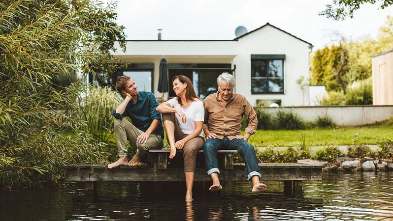 Eine Familie sitzt glücklich vor ihrem neuem Haus am See