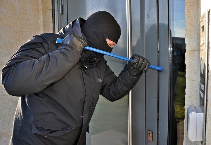 ein Maskierter Mann versucht mit einer Brechstange eine Tür aufzubrechen