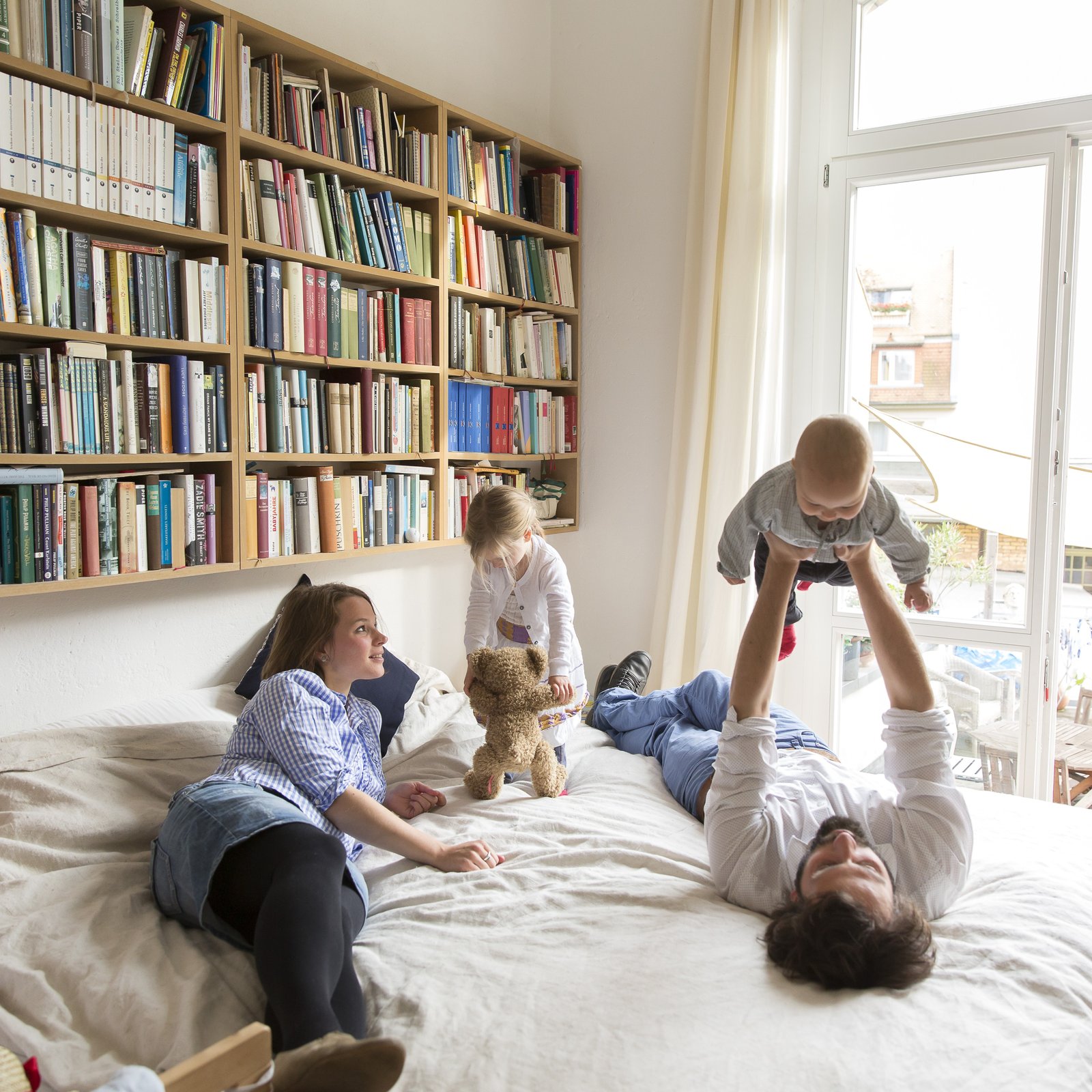Familie spielt fröhlich auf dem Bett in einer mit Kredit finanzierten Eigentumswohnung