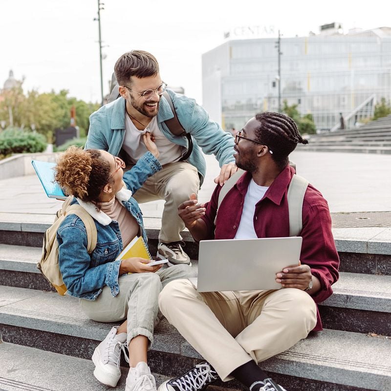 Studierende sitzen auf einer Treppe im Freien und haben Spaß