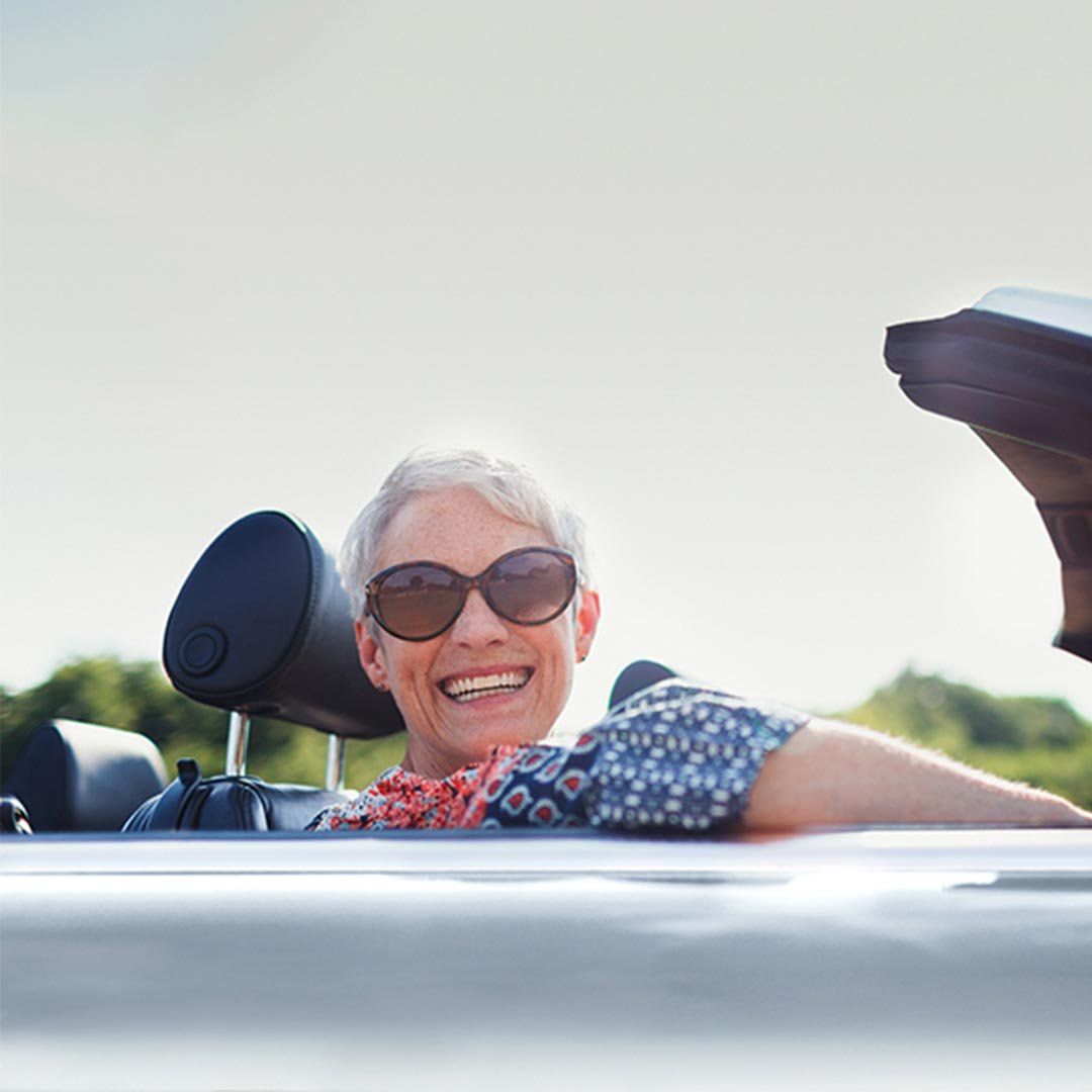 Eine ältere Dame sitzt in einem Sportwagen und lächelt in die Kamera