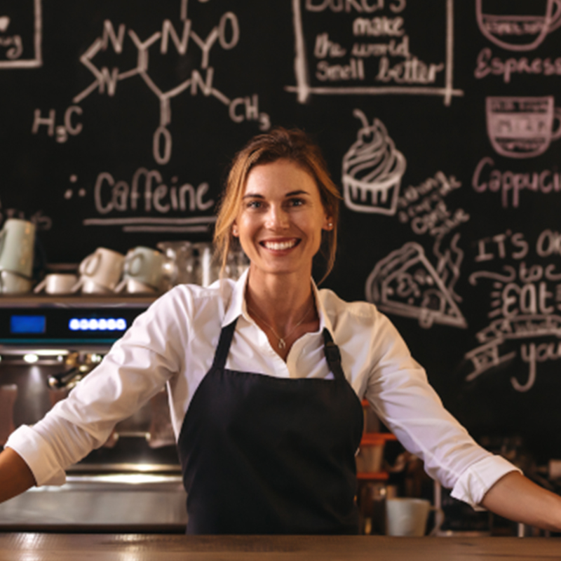Eine Barrista steht am Tresen und lächelt glücklich