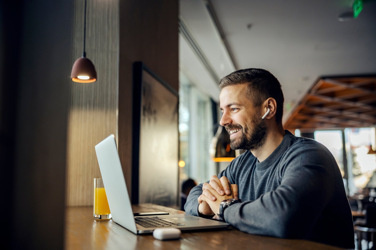 Männlicher glücklicher Kunde mittleren Alters, der sich mit kabellosen Kopfhörern vor dem Laptop im stylischen Ambiente beraten lässt.