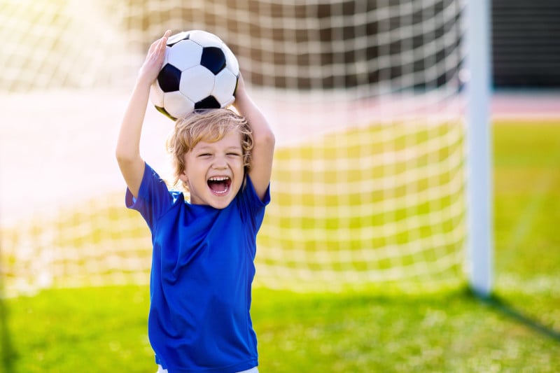 Ein Kind fängt mit viel Spaß einen Ball vor dem Fußballtor auf.