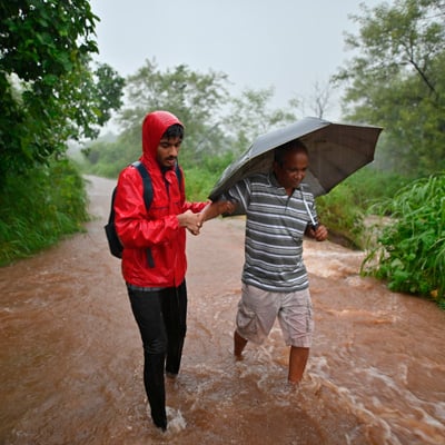 Young man holding his grandfather's hand and walking in stream while it's raining heavily 