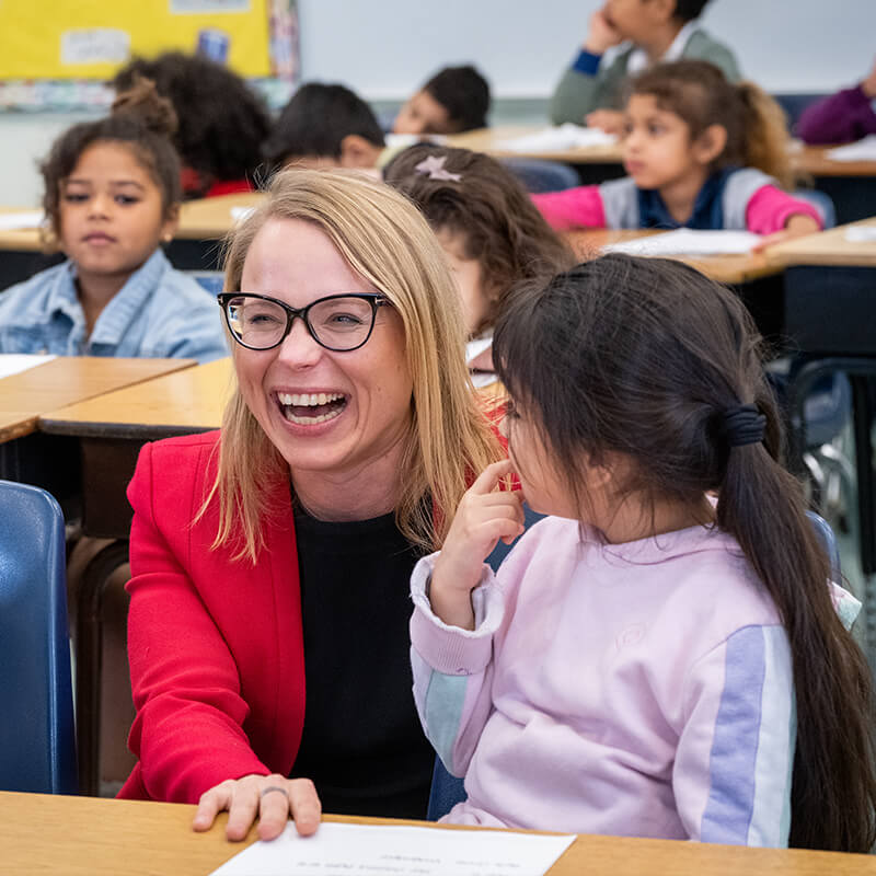 Woman with a girl on her lap laughing at school
